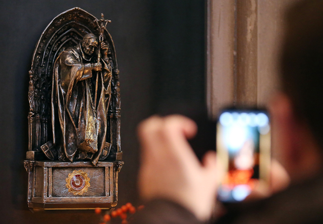 Picture taken on December 10, 2013 shows a tourist photographing a statue containing the relic of Pope John Paul II, in the Cologne cathedral, western Germany. A cloth with a drop of Pope John Paul II's blood was stolen from Cologne Cathedral in western Germany at from June 4 to 5, 2016 , police said. / AFP PHOTO / dpa / Oliver Berg / Germany OUT