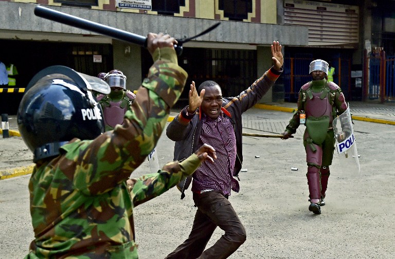 Kenyan riot police officers raise batons over a man during a demonstration of Kenya's opposition supporters in Nairobi, on May 16, 2016.  Opposition protestors led by former Prime Minister Raila Odinga gathered outside the Indepedent Electoral and Boundaries Comission building to demand the dismissal of IEBC commissioners, after alleged bias towards the ruling Jubillee Alliance Party. / AFP PHOTO / CARL DE SOUZA